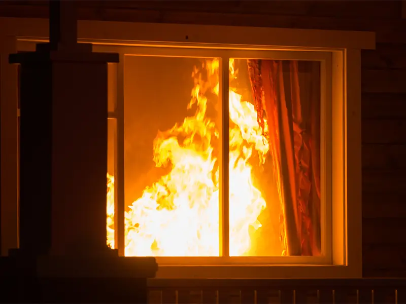 Exterior window shot of a raging fire inside a home. Best Cleanup offers Mecklenburg County fire damage restoration services 24/7.